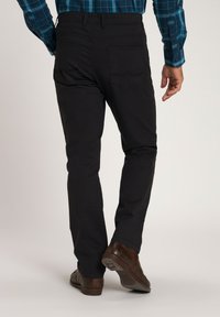 Schwarze Hose mit geradem Bein, ausgestattet mit Gesäßtaschen und einer glatten Textur. Getragen mit braunen Schuhen.