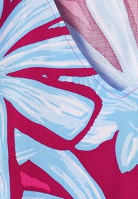 Tissu lumineux avec un grand motif floral abstrait en bleu clair, blanc et magenta, montrant une couture cousue et un coin plié.