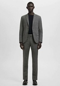 Traje de cuadros grises con blazer estructurado y pantalones de pierna recta. Combinado con una camiseta negra de cuello redondo y zapatos negros. Textura de tela lisa.