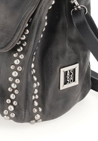 Zwarte leren tas met metalen studs langs één zijde, een flapluiting en een zilveren logo-plaatje. Zachte textuur met een slome vorm.