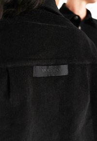 Zwarte corduroy shirt met een subtiele ribbelstructuur en een label met het "MULTIPLY"-logo op de achterkant van de hals.