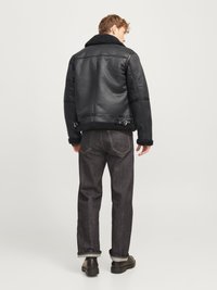 Crna kožna jakna s ovčjim krznom s visokim ovratnikom, bočnim kopčama i glatkom završnom obradom, uparena s tamnim trapericama i crnim cipelama.