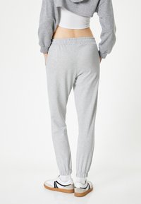 Grijze sweatpants met elastische tailleband en boorden, met een gladde textuur. Gedorven met witte en grijze sportschoenen.