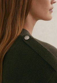 Tamnozeleni džemper s teksturiranim finišem, istaknuti srebrni gumb na ramenu i koso dizajnirani ovratnik.