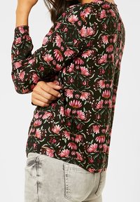 Blusa floreale con sfondo nero e motivi floreali rosa e verdi, maniche lunghe con polsini arricciati e scollatura tonda.