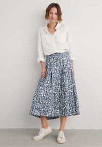 Sininen kukkainen hame, jossa valkoisia kuvioita, kellotettu malli, polvipituinen. Yhdistetty valkoiseen napitettuun paitaan ja kermaisiin tennareihin. Puuvillakangasta.