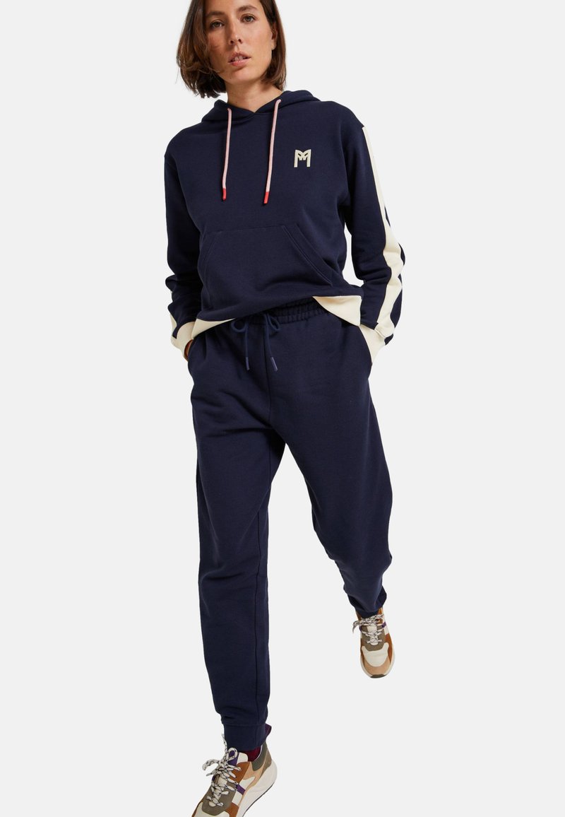 Sweatshirt à capuche marine avec des accents crème, poche avant et cordons de serrage ; assorti à un pantalon de jogging marine, avec taille élastique.