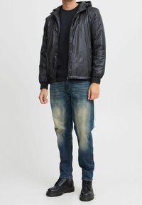 Schwarze, leichte Kapuzenjacke mit elastischen Bündchen, kombiniert mit ausgewaschenen blauen Jeans und schwarzen Schnürstiefeln. Einfaches, funktionales Design.