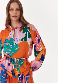 Färgglad blus med krage, långa ärmar och ihopdraget midja, med abstrakta mönster i orange, rosa, grön och blå.