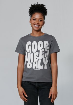Grijze katoenen t-shirt met een opvallende witte grafische tekst die zegt "GOEDE VIBES ALLEEN". Korte mouwen en een klassiek ronde hals ontwerp.