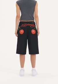 Pantalones cortos de mezclilla negra con cerezas rojas bordadas en los bolsillos traseros y el logo de "Ed Hardy", con un ajuste relajado y corte recto.