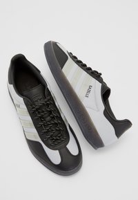 Black and white Adidas Gazelle sneakers featuring a textured fabric upper, black rubber sole, and striped accents on the sides.