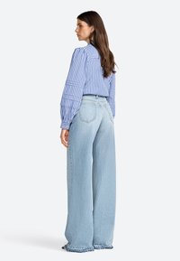 Jeans larges bleu clair avec ourlet effiloché, associés à un chemisier bleu et blanc à rayures avec des manches bouffantes et un détail de couture au dos.