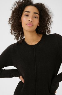 Pull en maille noir avec un col rond, des poignets côtelés et un détail de couture centrale subtil. Texture douce et coupe décontractée.