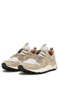 Sneakers beige e crema con una tomaia in tessuto testurizzato, dettagli in suede e un logo nero. Suola spessa con un motivo di battistrada robusto.