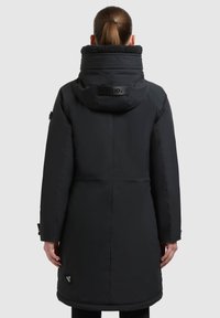 Chaqueta negra impermeable con un alto cuello, textura acolchada y detalle del logo en la parte posterior. Presenta un diseño de longitud media y cierres ajustables.