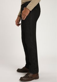 Schwarze gerade Hosen aus weichem Stoff, mit glatter Textur, dezenten Nähten und einem sicheren Knopfverschluss. Braune Schuhe runden den Look ab.