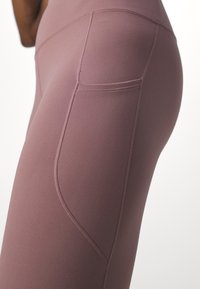 Legging taille haute, ajusté, dans une couleur mauve douce. Comprend une poche sur le côté droit et une texture lisse avec des coutures plates.