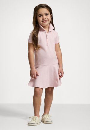 Vestito polo rosa realizzato in un tessuto morbido, con colletto, maniche corte e gonna svasata; indossato con sneakers di colore chiaro.