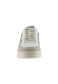 Sneaker bianco con accenti in suede beige chiaro e teal. Presenta una punta perforata, lacci beige e un'etichetta con logo sulla linguetta. Suola piatta.