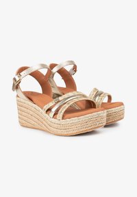 Sandalias de cuña con tiras doradas y suelas de cuerda trenzada, que presentan una plantilla acolchada en tono marrón y tiras metálicas para un detalle adicional.