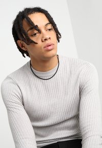 Light gray ribbed long-sleeve shirt with a fitted design. Black layered necklace visible around the neck. Simple, textured fabric.