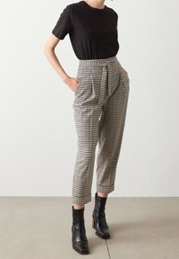 Černé tričko s krátkým rukávem, doplněné o kalhoty s vysokým pasem v kostičkovaném vzoru v béžové, hnědé a černé barvě, které mají boční kapsy a svázaný pas.