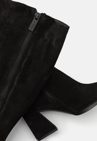 Černé semišové kotníkové boty s strukturální úpravou, vybavené bočním zipem a masivním podpatkem. Design je elegantní a moderní.