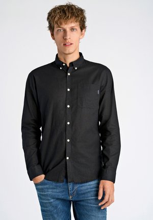 Zwarte overhemd met knopen, gemaakt van textuurstof, met een borstzak en witte knopen. Gepaard met blauwe jeans.