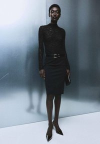 Černý krajkový top s dlouhým rukávem v kombinaci s úzkou černou sukní s páskem. Lesklé černé lodičky na vysokém podpatku a černá kabelka dotváří celý vzhled.