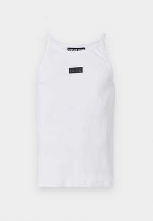 White cotton tank top with thin straps, featuring a small rectangular black logo patch at the center. Smooth texture, simple design.