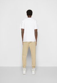 Bílý tričko s krátkým rukávem a béžové tepláky. Tepláky mají zúžený střih. Oblečení je doplněno bílými vysokými teniskami.