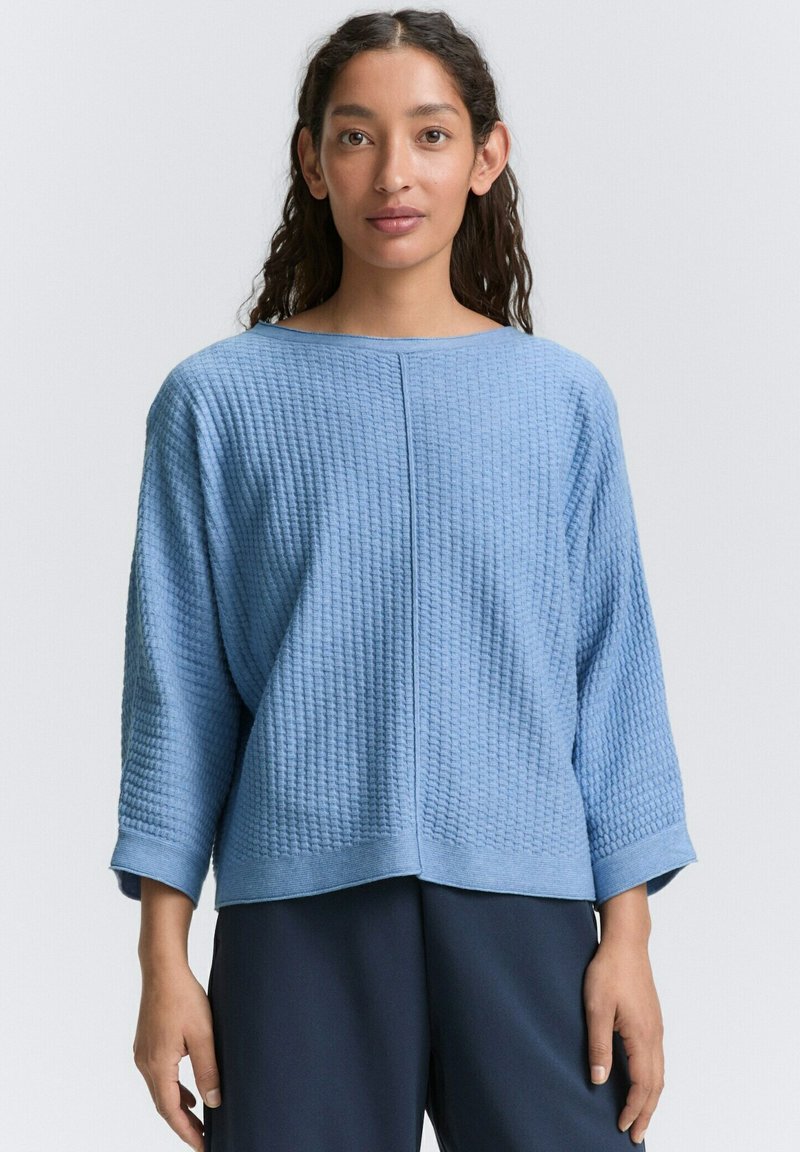 Maglione azzurro chiaro in tessuto strutturato con maniche a tre quarti e vestibilità rilassata. Presenta una cucitura orizzontale al centro e polsini a coste.