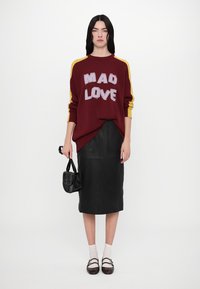 Burgundy knitted sweater with "MAD LOVE" text, yellow shoulder stripes; paired with a fitted black leather skirt, black shoes, and small bag.