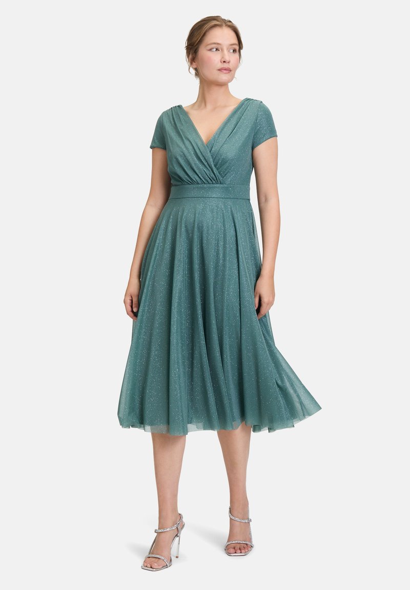 Robe en tulle verte avec un décolleté en V et des manches courtes, présentant une taille ajustée et une jupe fluide ornée de subtiles paillettes.