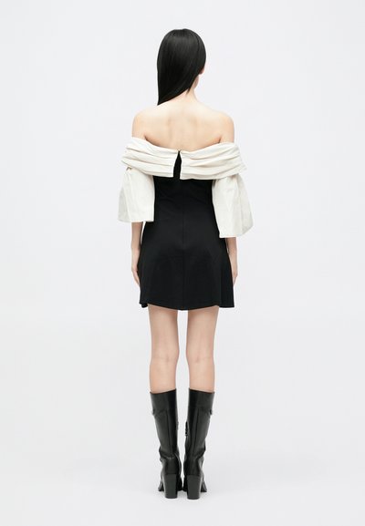 Haljina bez ramena s prilagođenim crnim korzetom i bijelim napuhanim rukavima, s patentnim zatvaračem straga i uparenim s čizmama do koljena u crnoj boji.