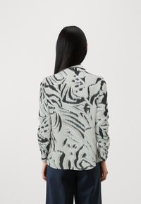 Langärmlige Bluse in Hellgrau mit schwarz abstraktem Muster. Verfügt über einen spitzen Kragen und Knopfdetails an den Manschetten. Weicher Stoff.