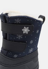 Botte d'hiver bleu marine avec une douce doublure blanche, ornée de motifs argentés de flocons de neige et de bandes Velcro noires pour la fermeture. Semelle en caoutchouc durable.
