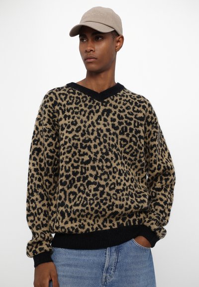 Animal print knit sweater in beige and black, featuring a V-neck, ribbed cuffs, and hem. Paired with light blue denim.