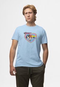Camiseta de algodón azul claro con un diseño gráfico que presenta tres personajes de dibujos animados en forma de corazón, enmarcados con un contorno multicolor.