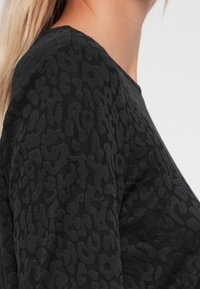 Schwarzes Langarmtop mit einem strukturierten Leopardenmuster, aus glattem Stoff und mit einem Rundhalsausschnitt.