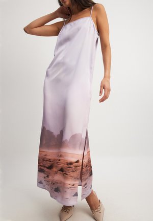 Satin glidkjole i blød lavendel med et fotografisk landskabsprint ved kanten. Har spaghetti-stropper og en sideskæring.