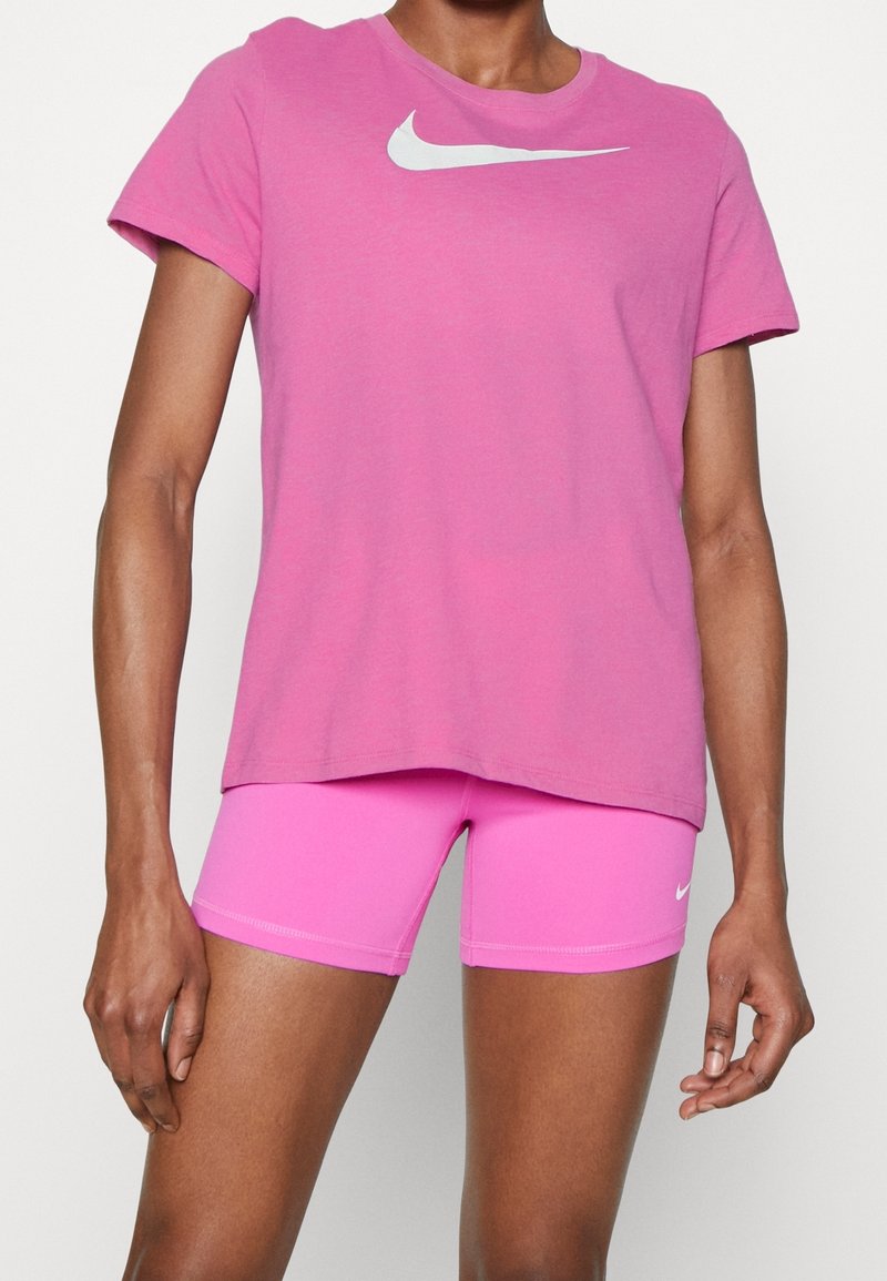 Růžové tričko Nike s krátkým rukávem a bílým logem, v kombinaci s odpovídajícími růžovými sportovními šortkami, které mají hladkou texturu.