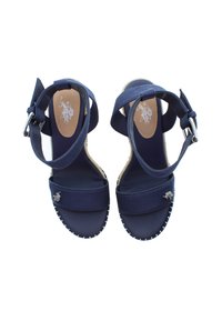 Námořnické modré espadrilky na klínku s páskem kolem kotníku, svršek ze semiše, gumová podrážka a stříbrné logo na přední části a vnitřní podrážce.