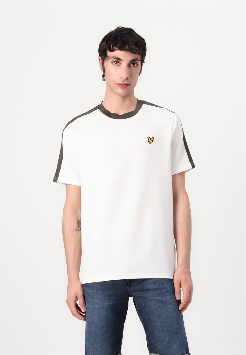 Vit bomull t-shirt med olivgrön krage och axelaccenter, med en liten gul fjärilslogotyp på vänster bröst.