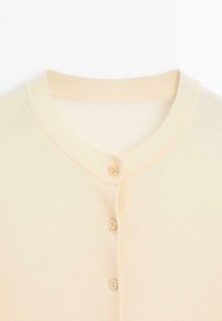 Helle beigefarbene Strickjacke mit rundem Ausschnitt, ausgestattet mit fünf passenden Knöpfen und weichem, strukturiertem Stoff. Schlichte und klassische Gestaltung.