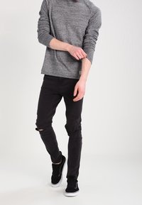 Grå texturerad långärmad skjorta med raglanärmar, i kombination med svarta slim-fit jeans med hål vid knäet, och svarta sneakers.