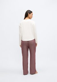 Krēmkrāsas garām piedurknēm topi ar apaļu apakšmali un vaļēju piegriezumu, kombinēts ar burgundu vertikāli svītrainām, platām biksēm. Nav izteiktu detaļu vai dekoratīvu elementu.