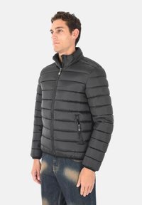 Giacca a vento nera con colletto alto, design trapuntato, zip frontale e tasca laterale; realizzata in materiale leggero e liscio.