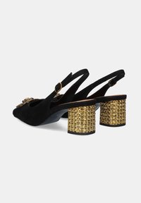 Zapatos slingback de ante negro con un elemento decorativo en la parte frontal y tacones de bloque con tachuelas doradas. Correa ajustable con hebilla redonda.